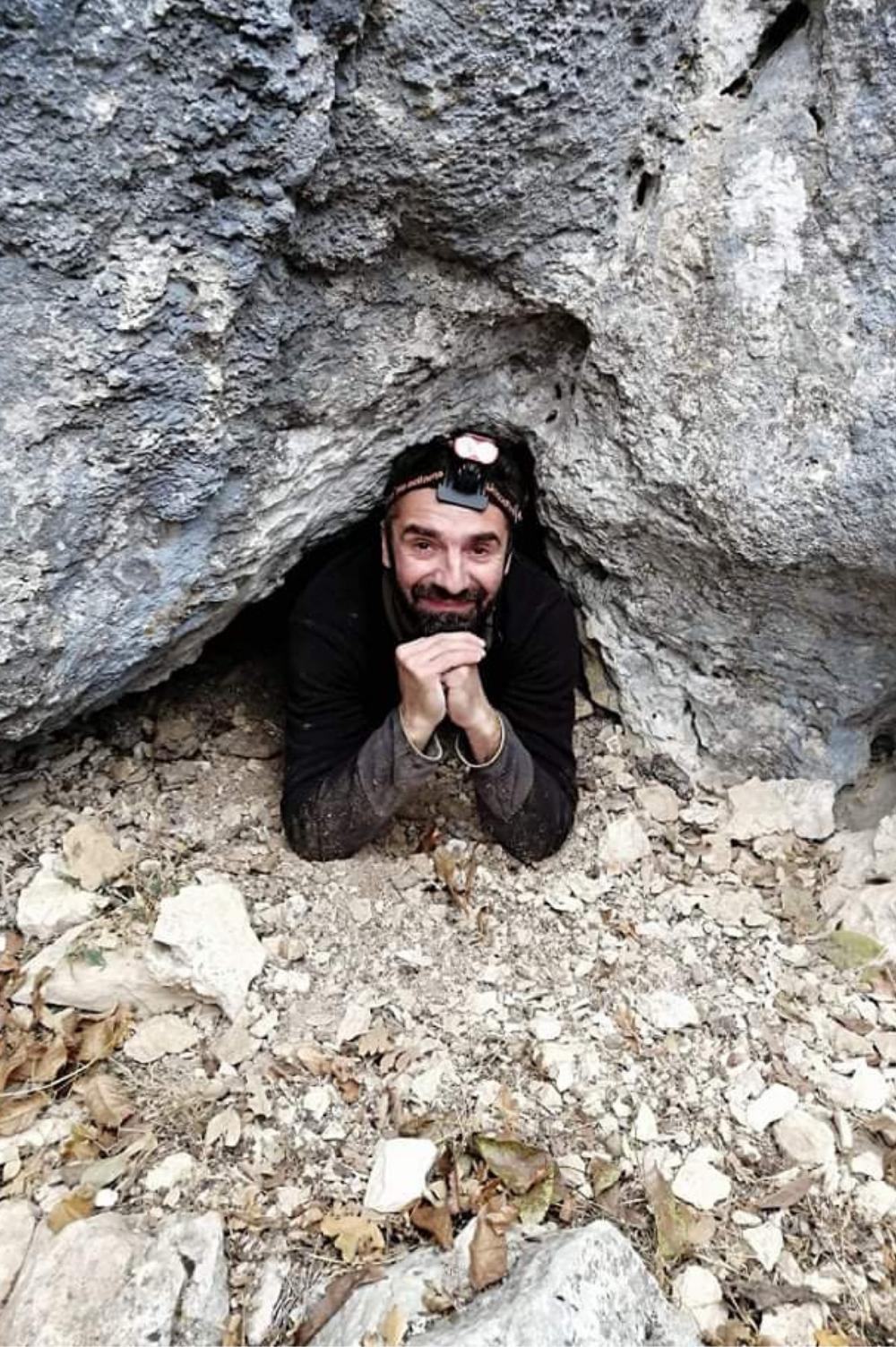 Dečko u opremi za istrazivanje pećina viri iz jedne male pećine.